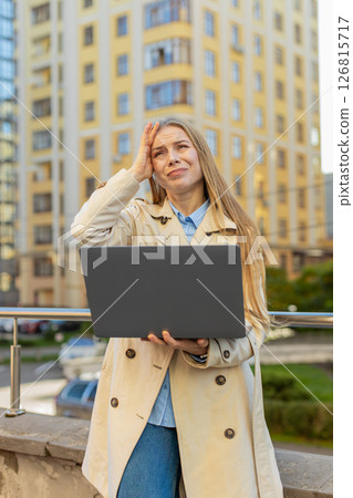 Mature Caucasian woman on laptop in downtown street sees bad lottery results, looking disappointed Mature Caucasian woman on laptop in downtown street sees bad lottery results, looking disappointed 126815717