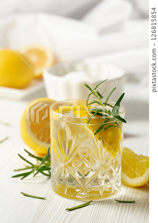 Summer refreshing lemonade drink or alcoholic cocktail with ice, rosemary and lemon slices on the white table. 126815854