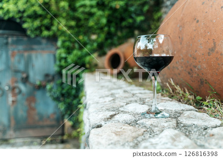 Glass of Red Wine with Traditional Georgian Qvevri in Rustic Setting 126816398
