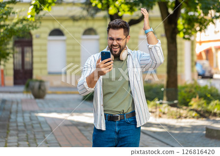 Upset young man using smartphone typing browsing, loses becoming shocked bad news on city street Upset young man using smartphone typing browsing, loses becoming shocked bad news on city street 126816420