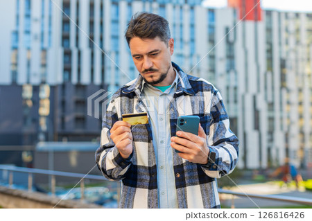 Frustrated mature businessman using credit card and mobile phone standing on downtown city street Frustrated mature businessman using credit card and mobile phone standing on downtown city street 126816426