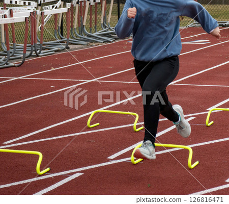 Runner Training With Mini Hurdles on a Red Track Field During Practice 126816471