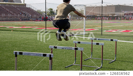 Athlete Training by Jumping Over Hurdles on a Sports Field Athlete Training by Jumping Over Hurdles on a Sports Field 126816562