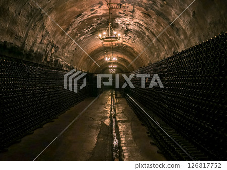 Dark underground wine cellar featuring endless rows of bottles illuminated by soft chandeliers Dark underground wine cellar featuring endless rows of bottles illuminated by soft chandeliers 126817752