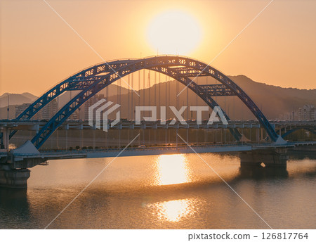 Evening panorama of a blue arch bridge with moving cars over calm water at sunset. Hangzhou, China. 126817764