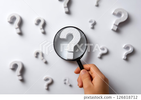 Question Mark and Root Cause Analysis Concept. A hand holding a magnifying glass over a large question mark surrounded by smaller ones on a blue background, symbolizing analysis and problem-solving. 126818712