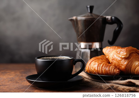 A fresh, white croissant and black coffee on a plate, a delicious French breakfast. A fresh, white croissant and black coffee on a plate, a delicious French breakfast. 126818756