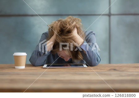 Young professional woman experiencing stress and burnout while working in a modern office, covering her face with hands and struggling with a difficult task or deadline. 126818800