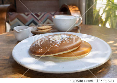 Tasty fluffy pancakes served with coffee and biscuits at a cozy cafe in the morning sunlight. Sweet homemade cakes on a white plate in close-up. 126820984