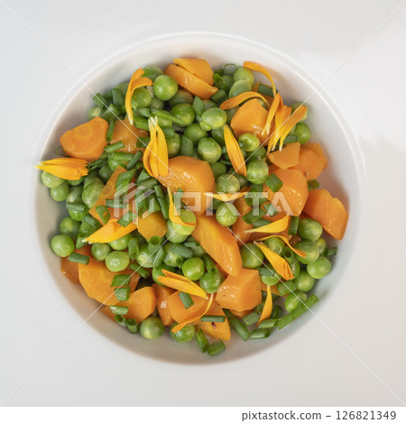 Fresh garden peas and carrots cooked in butter, garnished with chives and marigold flowers for a 126821349
