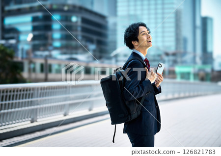 A businessman in a suit carrying a backpack operating a smartphone 126821783