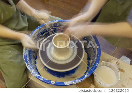 Earthenware on a potter's wheel and the hands of a potter, blurred in motion. Pottery training. 126822033