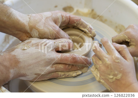 The potter teaches the craft to the child. Close-up of a potter's hands and a child's hand with a product on a potter's wheel. Working with clay. Clay master class. 126822036