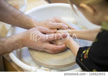 The potter teaches the craft to the child. Close-up of a potter's hands and a child's hand with a product on a potter's wheel. Working with clay. Clay master class. The potter teaches the craft to the child. Close-up of a potter's hands and a child's hand with a product on a potter's wheel. Working with clay. Clay master class. 126822052