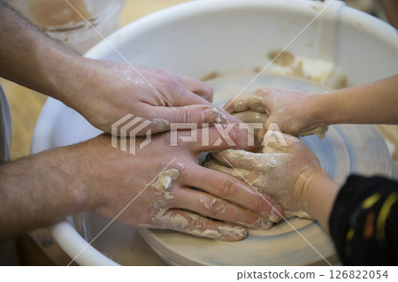 The potter teaches the craft to the child. Close-up of a potter's hands and a child's hand with a product on a potter's wheel. Working with clay. Clay master class. The potter teaches the craft to the child. Close-up of a potter's hands and a child's hand with a product on a potter's wheel. Working with clay. Clay master class. 126822054