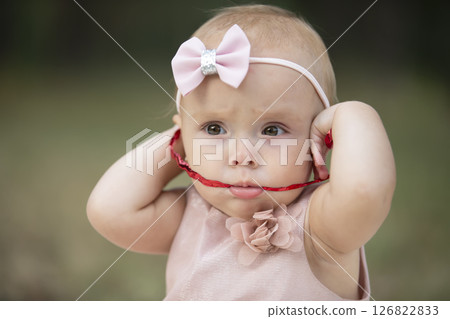 The funny girl took a red ribbon in her mouth. One year old child. A cute baby. 126822833