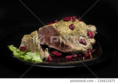 A piece of boiled meat with greens and cranberries on a black background. A piece of boiled meat with greens and cranberries on a black background. 126822875
