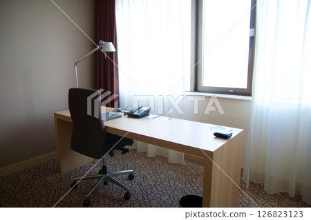 Mainz, Germany, July 7, 2017: Hotel Room Desk with Telephone, Lamp, and Chair by the Window Mainz, Germany, July 7, 2017: Hotel Room Desk with Telephone, Lamp, and Chair by the Window 126823123