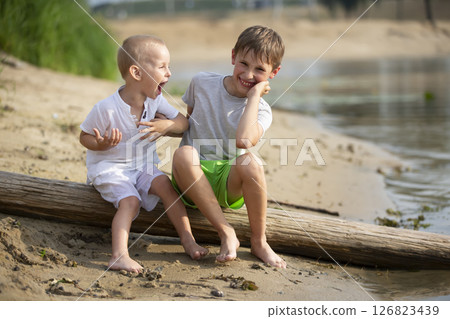 Two brothers, the elder and the younger, are playing by the river. Children on the sandy shore talk and indulge. 126823439
