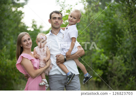 Husband and wife and their little children. Family portrait in nature. Mom and Dad are posing with their brother and sister. Young family with children for a walk in the woods. 126823703