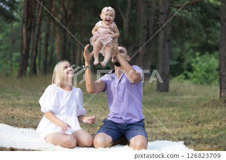 Husband, wife and their little daughter for a walk in the park. Happy dad and mom toss up their little daughter. 126823709