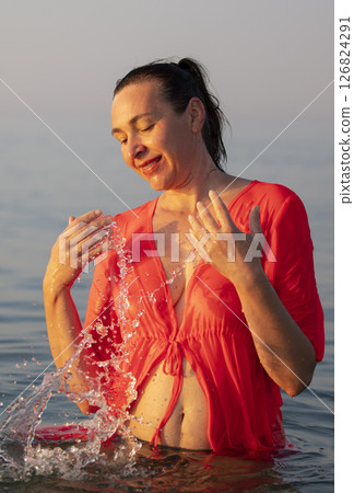 Beautiful elderly woman bathes in the sea and splashes water. 126824291