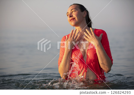 Beautiful elderly woman bathes in the sea and splashes water. 126824293