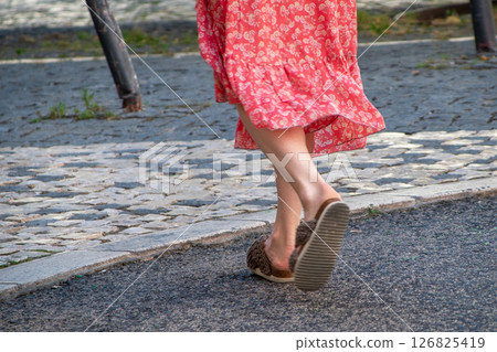 Woman in red floral dress and sandals walking on a stone pavement Woman in red floral dress and sandals walking on a stone pavement 126825419