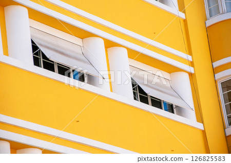 Bright yellow building facade with white pillars and window awnings 126825583
