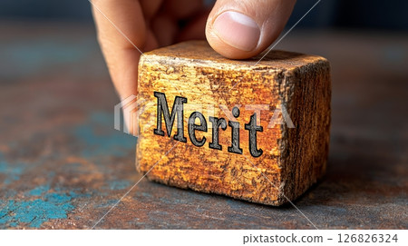 Fingertip Touching Weathered Wooden Cube with Engraved Merit on Rustic Metal Background 126826324