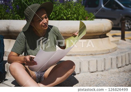 Traveler Sitting Outdoors Exploring a Map on a Sunny Day Traveler Sitting Outdoors Exploring a Map on a Sunny Day 126826499