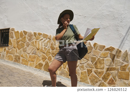 Adventurer Exploring a Picturesque Village with Map in Hand and Sun Hat 126826512