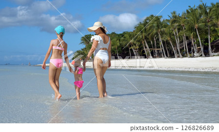Mom walks with daughters in ocean water during tropical vacation under blue sky 126826689