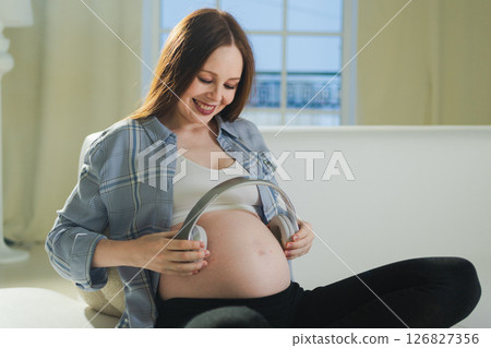 Pregnancy motherhood. Pregnant woman holding headphones near belly listening music for mother and unborn baby. Girl enjoying pregnancy listen music for relax calm wellness. Prenatal music stimulation Pregnancy motherhood. Pregnant woman holding headphones near belly listening music for mother and unborn baby. Girl enjoying pregnancy listen music for relax calm wellness. Prenatal music stimulation 126827356