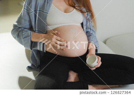 Pregnancy motherhood. Pregnant woman applying cream lotion on big belly takes care of her skin. Cosmetic product for prevention stretch mark. Girl enjoying pregnancy at home. Maternity health concept Pregnancy motherhood. Pregnant woman applying cream lotion on big belly takes care of her skin. Cosmetic product for prevention stretch mark. Girl enjoying pregnancy at home. Maternity health concept 126827364
