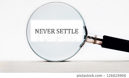 Concept words NEVER SETTLE focused through a magnifying glass 126828908