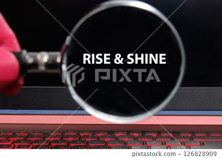 Growth Success Achievement Progress Concept. Words RISE AND SHINE through a magnifying glass on a laptop screen in a dimly lit room 126828909