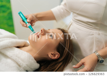 Closeup face of pretty female patient receiving rejuvenation treatment in cosmetology clinic. Professional beautician performing mesotherapy treatment to woman focusing on skin rejuvenation, hydration Closeup face of pretty female patient receiving rejuvenation treatment in cosmetology clinic. Professional beautician performing mesotherapy treatment to woman focusing on skin rejuvenation, hydration 126829363
