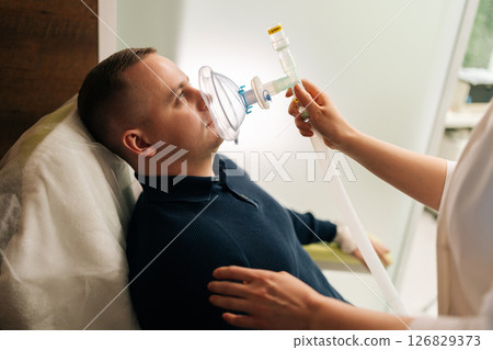Doctor touching male patient shoulder while administering oxygen through mask during respiratory training session, promoting improved breathing techniques and lung capacity. 126829373