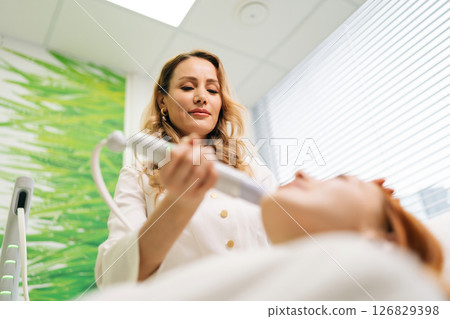 Female client getting mesotherapy treatment in clinic of aesthetic medicine. Beautician device to mesotherapy treatment on woman chin, close-up, low angle view. Concept of anti-age skincare. Female client getting mesotherapy treatment in clinic of aesthetic medicine. Beautician device to mesotherapy treatment on woman chin, close-up, low angle view. Concept of anti-age skincare. 126829398