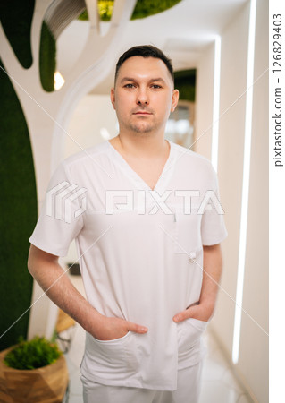 Confident male masseur standing with hands in pockets in modern spa center, showcasing professionalism and expertise in wellness and body care. Concept of body and health care, alternative medicine. Confident male masseur standing with hands in pockets in modern spa center, showcasing professionalism and expertise in wellness and body care. Concept of body and health care, alternative medicine. 126829403