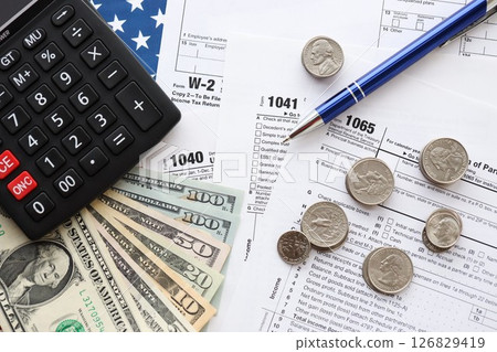 American US dollars money bills and coins with pen and calculator on IRS tax form blanks American US dollars money bills and coins with pen and calculator on IRS tax form blanks 126829419