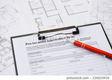 Pen on pre-tenancy application form and planning blueprints of residential building project close up 126829430