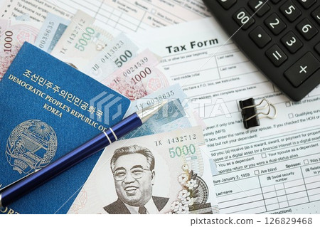 North Korean won money bills lies on table with pen, calculator, passport and tax forms 126829468