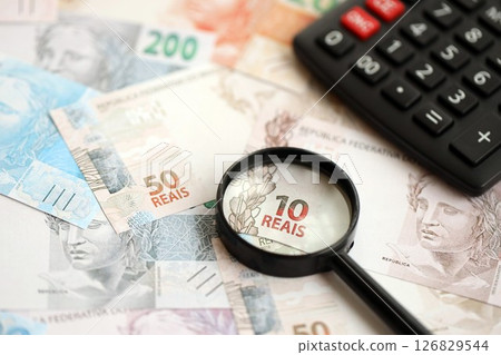 Brazilian reais banknotes and calculator with magnifying glass. Brazil real money, calc with loupe Brazilian reais banknotes and calculator with magnifying glass. Brazil real money, calc with loupe 126829544