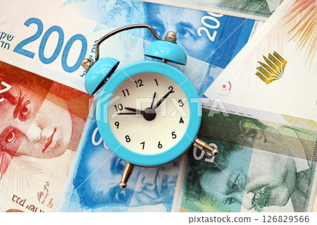 Israel New Shekels banknotes and alarm clock. The current Israel money bills and clock lies on table Israel New Shekels banknotes and alarm clock. The current Israel money bills and clock lies on table 126829566