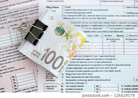 Israel New Shekels banknotes on tax form blank. The current Israel money bills lies on tax report Israel New Shekels banknotes on tax form blank. The current Israel money bills lies on tax report 126829579