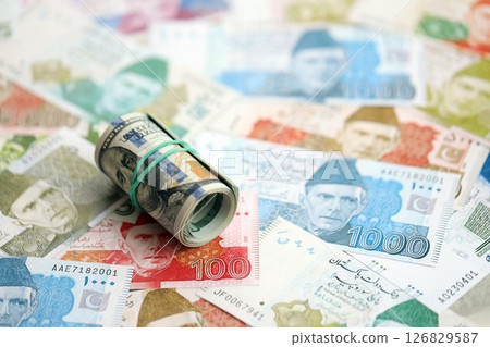 Roll of US dollar bills lies on big amount of Pakistan rupees banknotes close up Roll of US dollar bills lies on big amount of Pakistan rupees banknotes close up 126829587