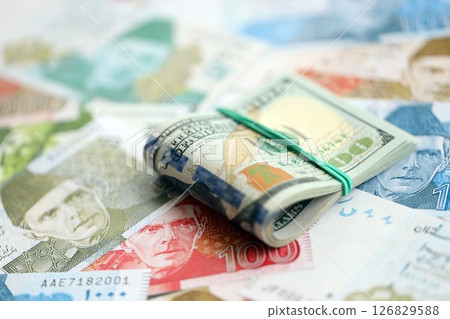 Bunch of US dollar bills lies on big amount of Pakistan rupees banknotes close up 126829588