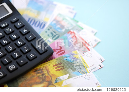 Swiss franc banknotes and calculator on blue. The current francs money bills and calc lies on table Swiss franc banknotes and calculator on blue. The current francs money bills and calc lies on table 126829623
